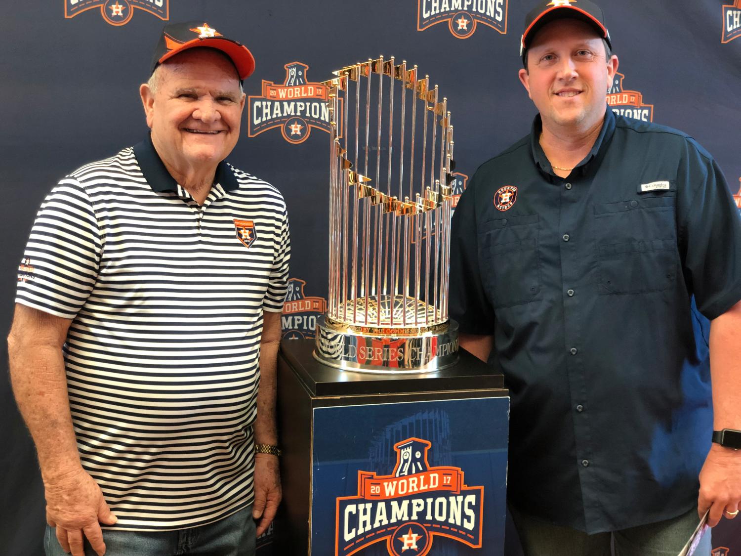 Father and son standing in front of the mlb world series trophy